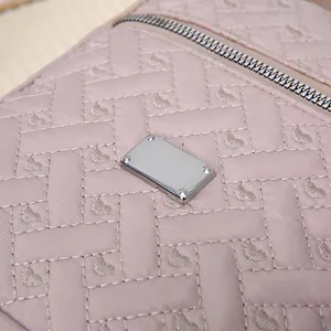 Close-up of pink quilted embroidery fabric with silver metal logo plate and zipper detail