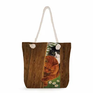 Detail of canvas tote bag with thick rope handles and cat pattern on wood grain background