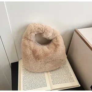 Detail of soft khaki faux fur dumpling bag with knot handle next to a book