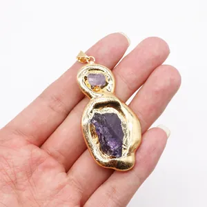 Detailed view of hand holding a raw purple crystal pendant with gold electroplated edge