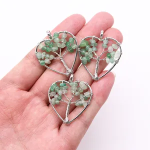 Detailed view of handmade silver wire heart pendants with green natural stones on hand