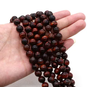 Dettaglio di perle di occhio di tigre rosso sulla mano con lucentezza naturale per gioielli