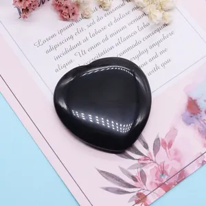 Polierter herzförmiger schwarzer Obsidian auf dekorativer Blumenkarte im Hintergrund