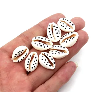 Close-up of handmade white cowrie shells with black polka dots held in palm for DIY jewelry
