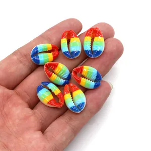 Rainbow striped cowrie shell beads for DIY jewelry making held in a person's palm