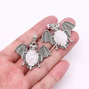Close-up of bat-shaped alloy pendants with natural stone inlay held in a hand
