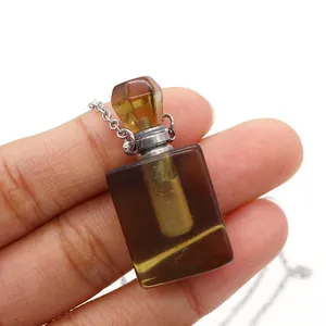 Macro detail of amber crystal perfume bottle pendant with silver chain held by hand