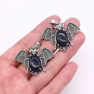 Detailed close-up of bat-shaped alloy pendants with blue sandstone inlay in hand