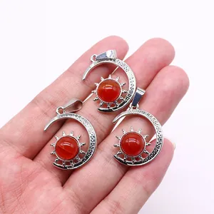 Detailed view of crescent moon and sun pendants with red stones held in hand