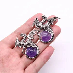 Detail of silver viking dragon pendants holding purple round gemstones held by hand