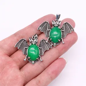 Detail of silver bat pendants with green stones held by hand to show size and texture