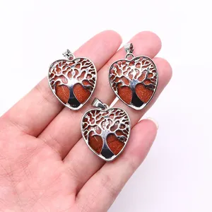 Detailed view of tree of life heart pendants with goldstone held by hand for scale