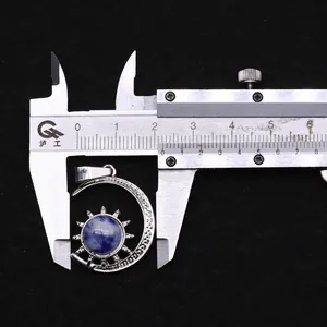 Measuring silver sun and moon pendant with a blue gemstone using a metal caliper