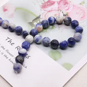 Φυσικές μπλε και λευκές χάντρες σοδολίτη για κοσμήματα DIY σε φόντο με λουλούδια