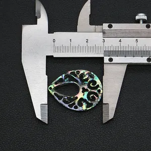 Macro detail of teardrop abalone shell pendant with floral carving on black background