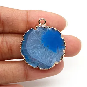 Dettaglio del ciondolo a fetta di agata blu con bordi placcati in oro tra le dita