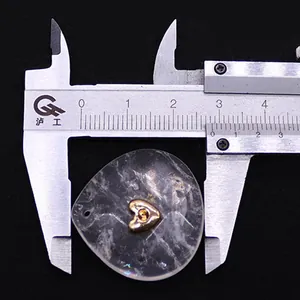 Caliper measuring 28mm width of a teardrop crystal pendant with gold heart inlay