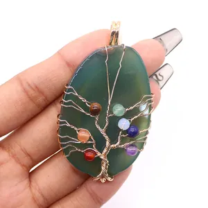 Detail van levensboom hanger met groene agaat en kleurrijke chakra kralen in de hand getoond