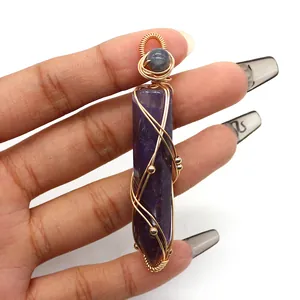 Macro detail of handmade gold wire-wrapped purple hexagonal crystal pendant in hand