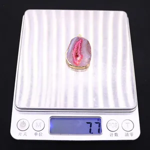 Vue macro d'un pendentif en agate rose de 7,7g avec bordure dorée posé sur une balance