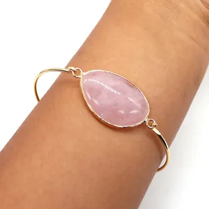 Detail of a gold plated open cuff bracelet featuring an oval pink quartz gemstone inlay