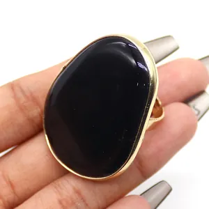 Detalle de un anillo dorado ajustable con una gran piedra natural negra en la mano de una modelo