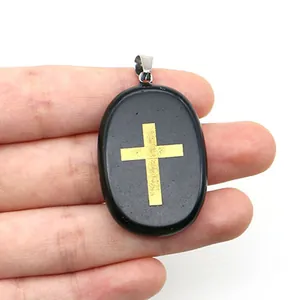 Gros plan d'un pendentif ovale en pierre noire avec une croix dorée tenu en main