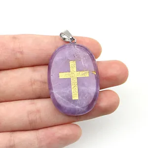 Vue détaillée du pendentif ovale en améthyste violette avec croix dorée en main