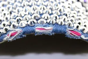 Makroaufnahme einer Denim-Kappe mit silbernen Nieten und rosa ausgefransten Stoffkanten