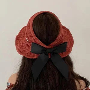 Detail of red knit sun visor featuring a large black satin bow and silver metal logo tag