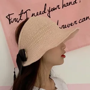 Detail of beige straw sun visor featuring a stylish black ribbon bow and wide brim