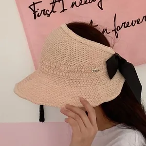 Detail of beige knitted visor hat featuring a large black bow and silver logo accent