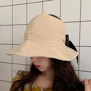 Detail of a beige woven straw sun hat featuring a wide brim and black silk bow accent