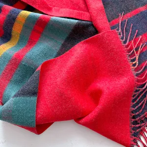 Macro view of red and green plaid wool shawl texture with colorful fringe tassel details