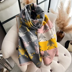 Bufanda bicolor de tacto cachemira con estampado de abejas y flecos en sofá