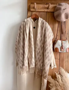 Detail showing geometric V-pattern knit texture and long tassels on a warm beige scarf