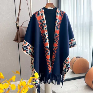 Ethnic knit poncho with geometric bohemian patterns and fringe detail on a wooden hanger