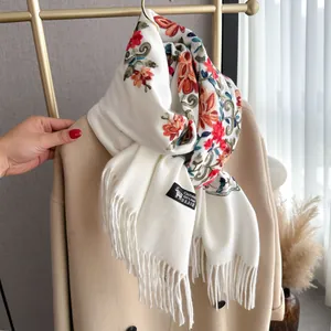 Detail of white wool scarf with colorful floral embroidery and long fringes on a coat