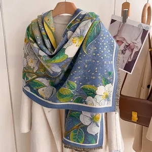 Close-up of blue winter scarf with white floral patterns and elegant grey fringe tassels