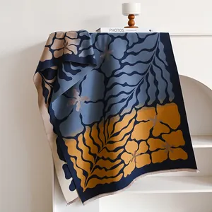 Winter floral cashmere shawl with tassel trim draped over a white minimalist bookshelf