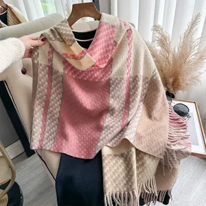 Detail of soft plaid cashmere-feel scarf with pink and beige fringe tassels hanging on a hanger