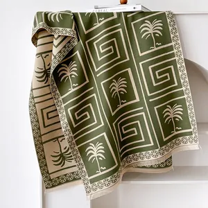 Detail of dark green and beige jacquard knit scarf showing palm tree texture and fringe edges