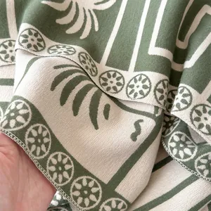 Close-up of olive green and beige jacquard knit scarf showing ethnic plant pattern