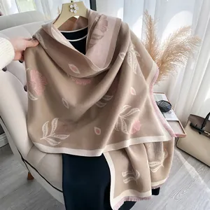 Floral cashmere-feel shawl with pink fringe tassels draped on a beige chair
