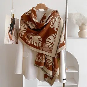 Détail d'une écharpe réversible à motif feuilles avec franges sur un blazer blanc