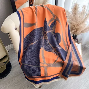 Detail of a thick orange equestrian shawl with horse head jacquard and fringe on leather sofa