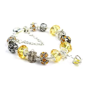 Detail of silver snake chain bracelet with yellow glass beads and a crown pendant charm