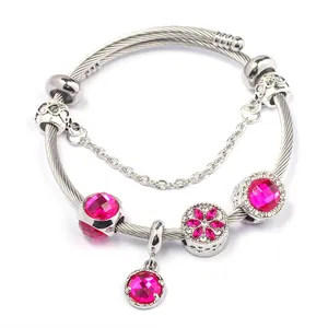 Dettaglio macro del bracciale argento a cavo con perline magenta e ciondolo floreale