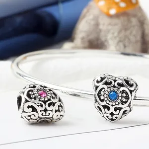 Macro detail of hollow heart bead charms with colorful gemstones and floral engravings