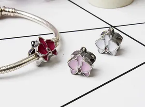 Detalle de dijes de orquídea esmaltada en color sobre pulsera de cadena de serpiente
